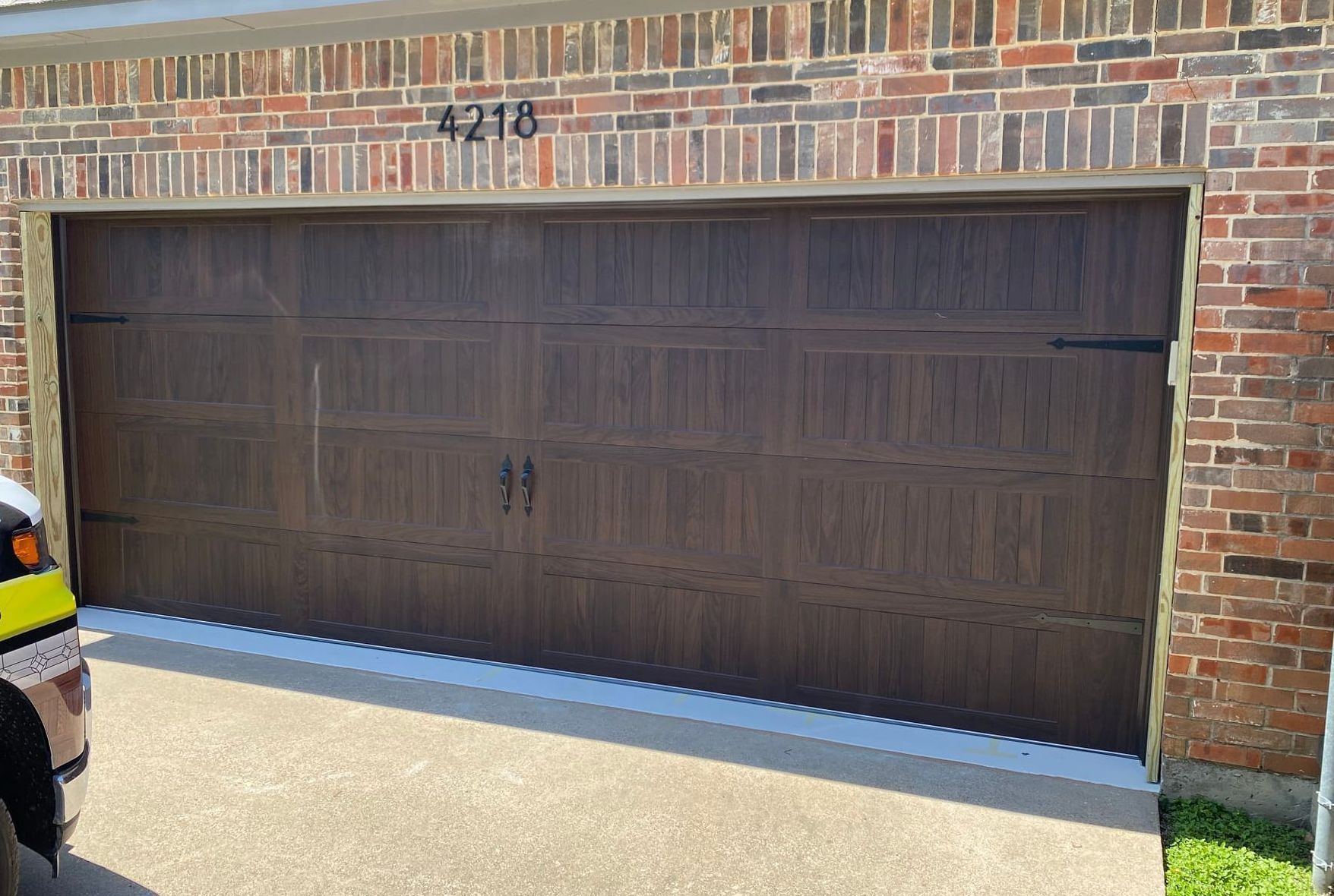 Brown garage door with black hardware, brick facade, and address number 