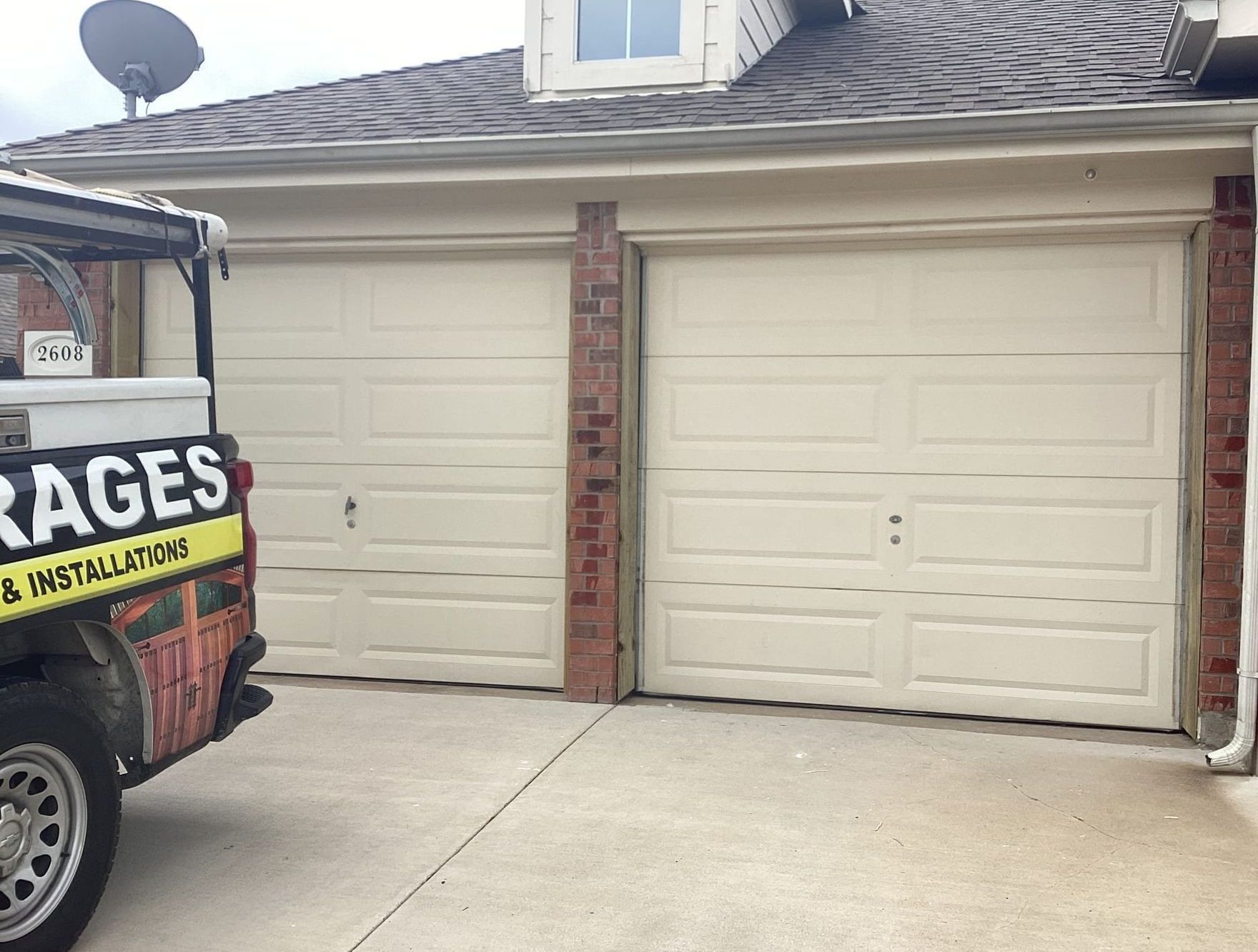 Two beige garage doors next to each other, with a brick pillar in between. A service vehicle is parked on the left.