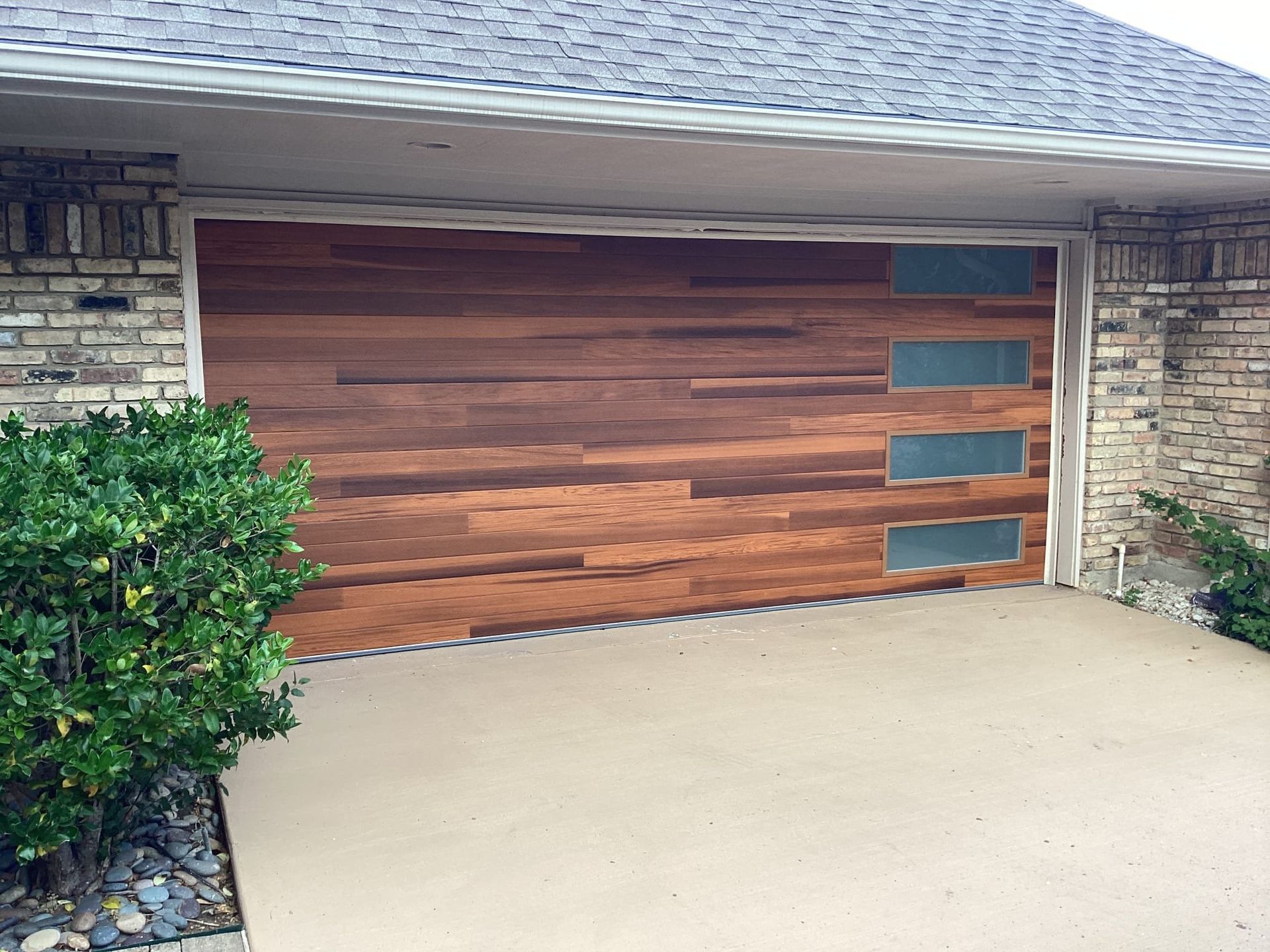Wooden garage door with three glass panels, brown and tan brick house.