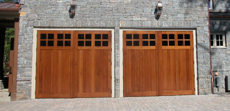 Two wooden carriage-style garage doors with windows, set into a stone exterior wall.