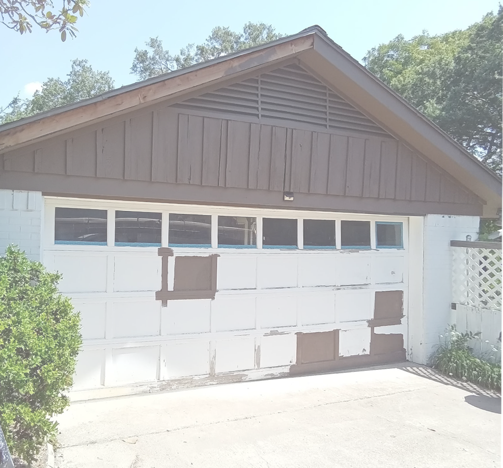 White garage door with peeling paint, brown trim, and a vent under the roof.
