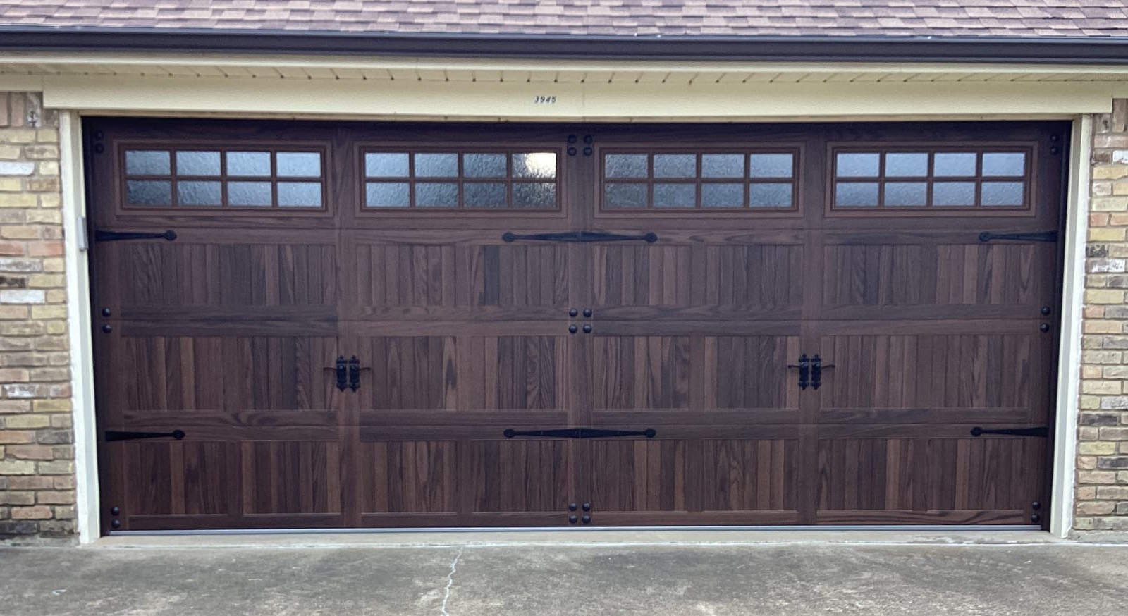 Brown garage door with windows, decorative hardware, brick facade.