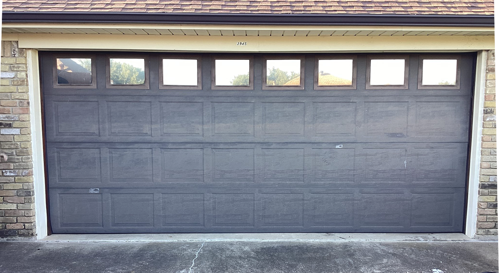 Gray garage door with eight small square windows across the top, set in a brick building.