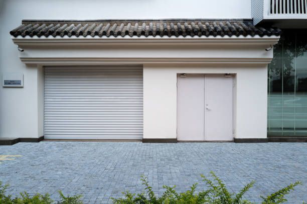 White building exterior with a roll-up door, double doors, and ornate trim beneath a tiled roof. White building exterior with a roll-up door, double doors, and ornate trim beneath a tiled roof.