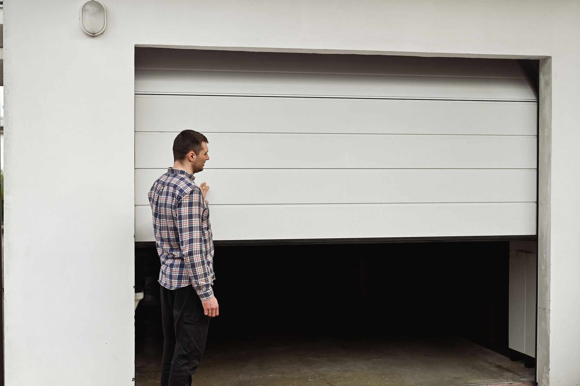 Man in plaid shirt watches a white garage door as it opens.