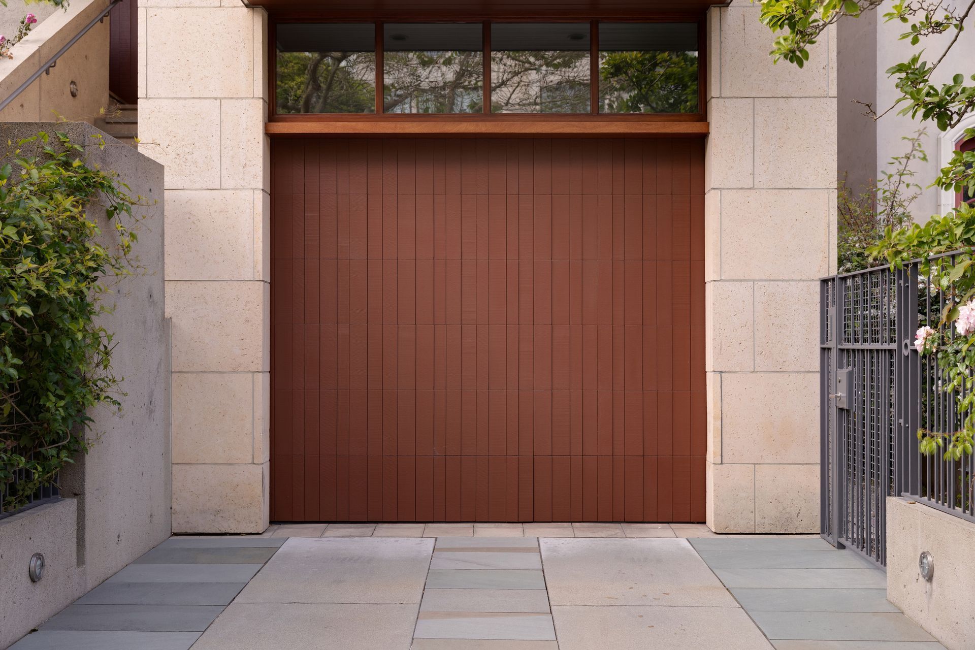 Brown garage door set in a stone facade, with a rectangular window above. A concrete driveway leads up.