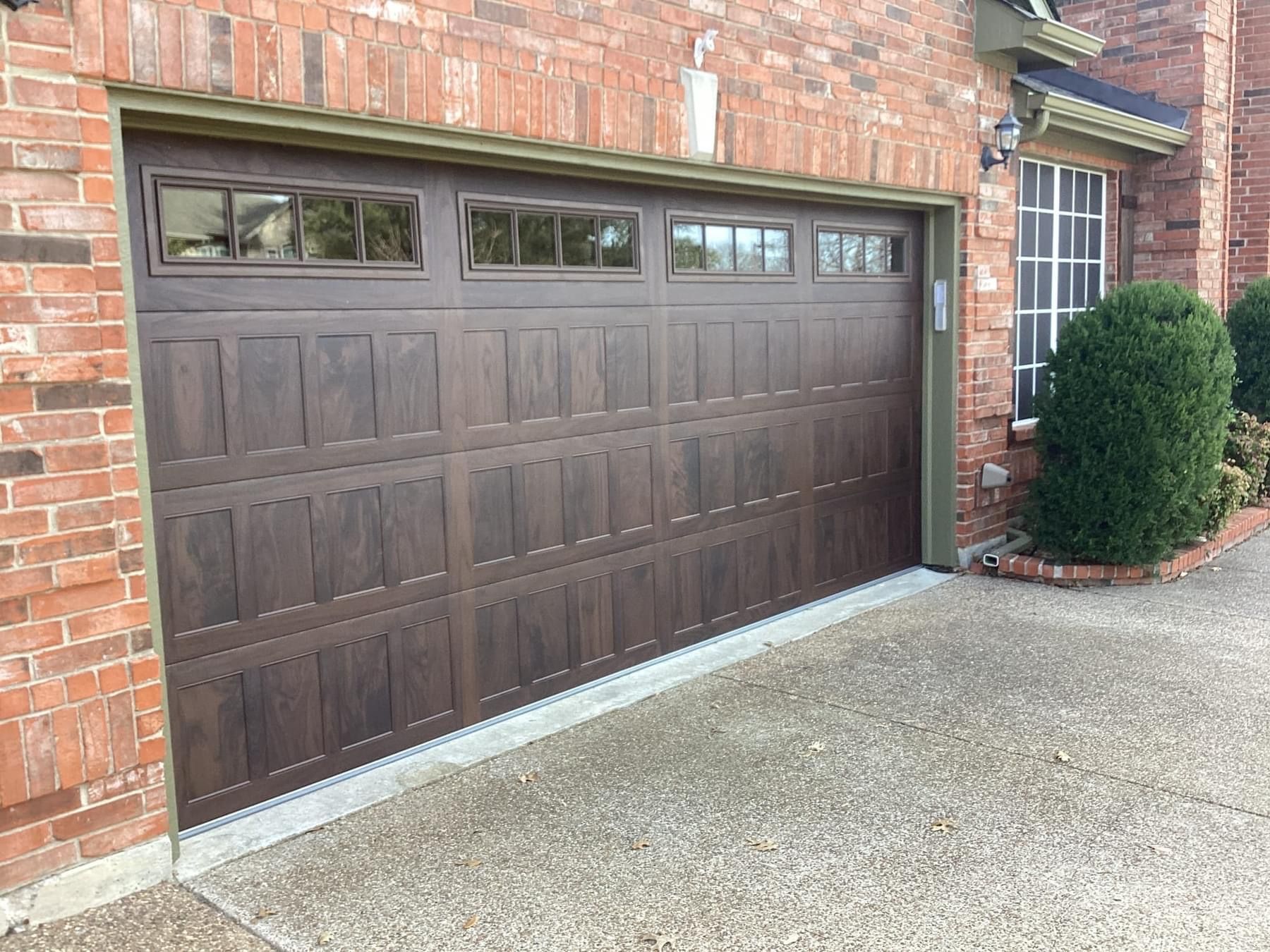 Dark brown garage door with rectangular window panels on a residential brick home.