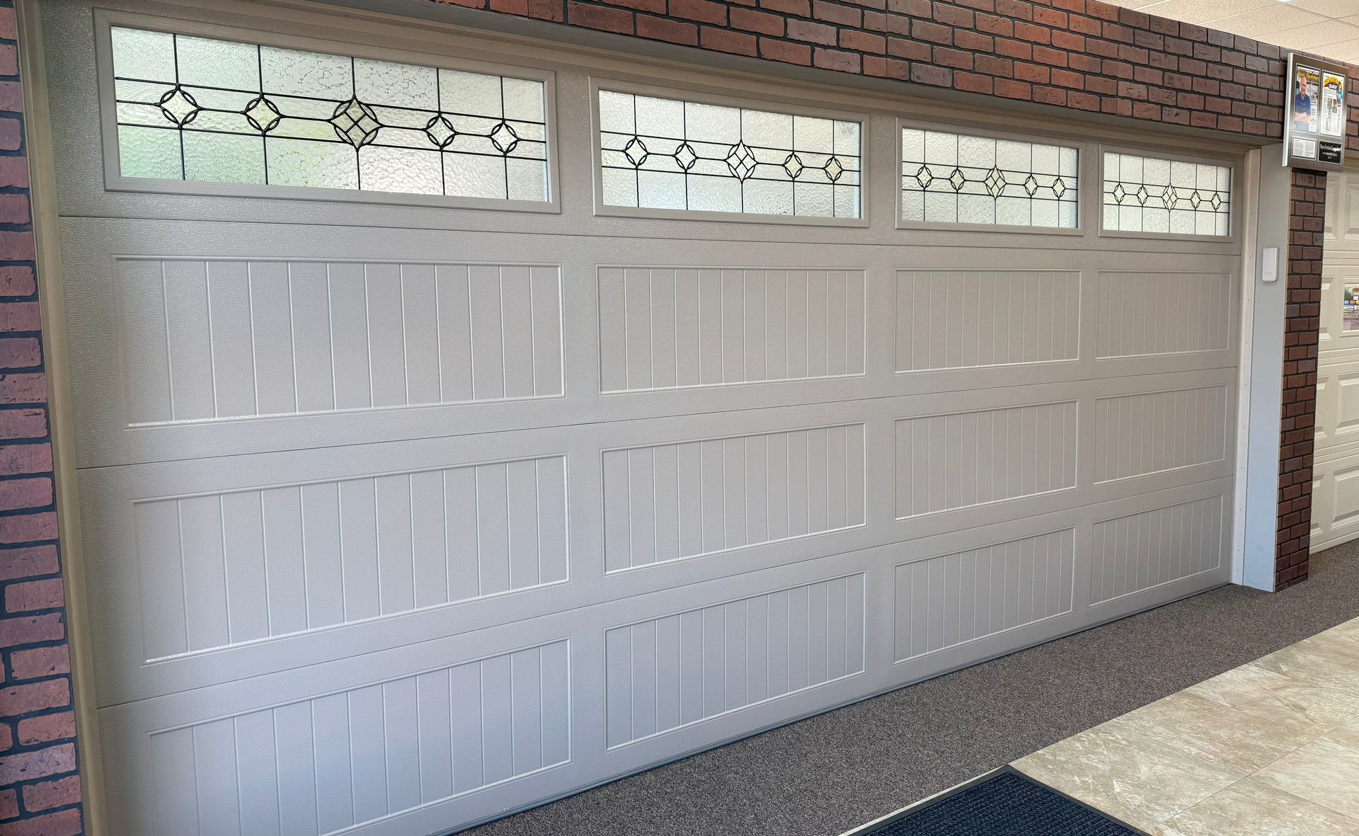 Beige garage door with decorative glass panels and brick exterior.