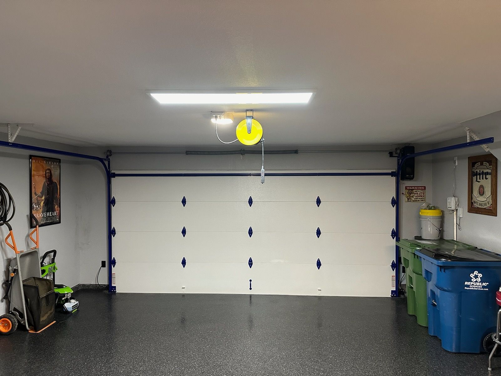 Garage interior with a closed white door, overhead light, and various tools.