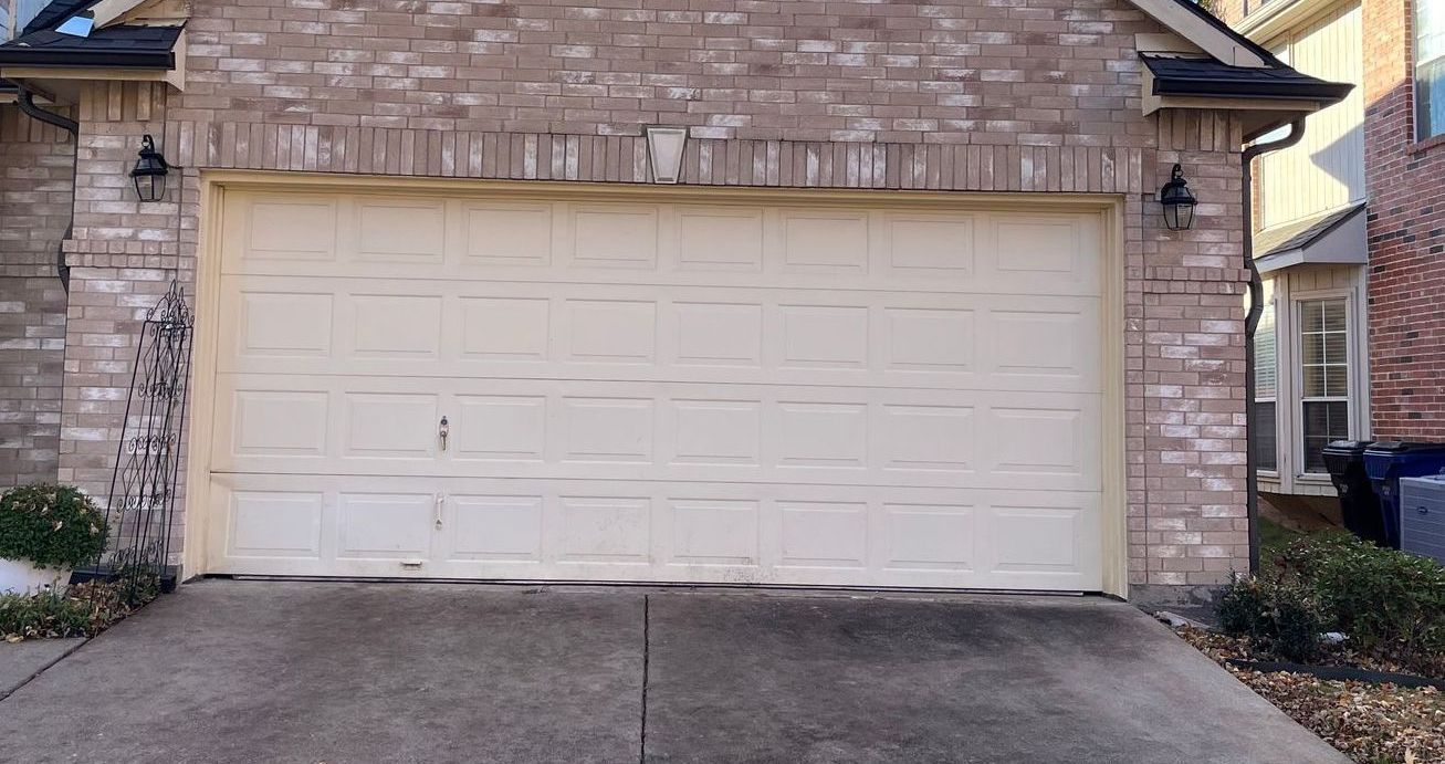 A closed beige garage door on a brick house.  Two black lamps flank the sides.  Concrete driveway in front.