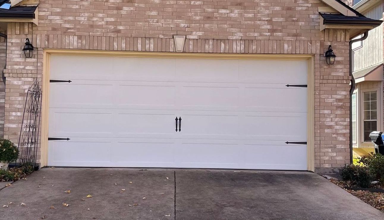 White garage door on a brick house, accented with black hardware, set in a concrete driveway.