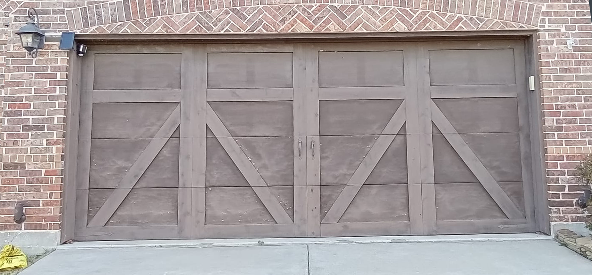 Brown wooden garage door with decorative diagonal beams, set against a brick wall.