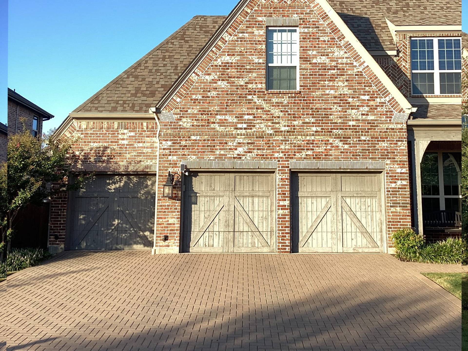 Brick home with three weathered garage doors on a brick driveway.