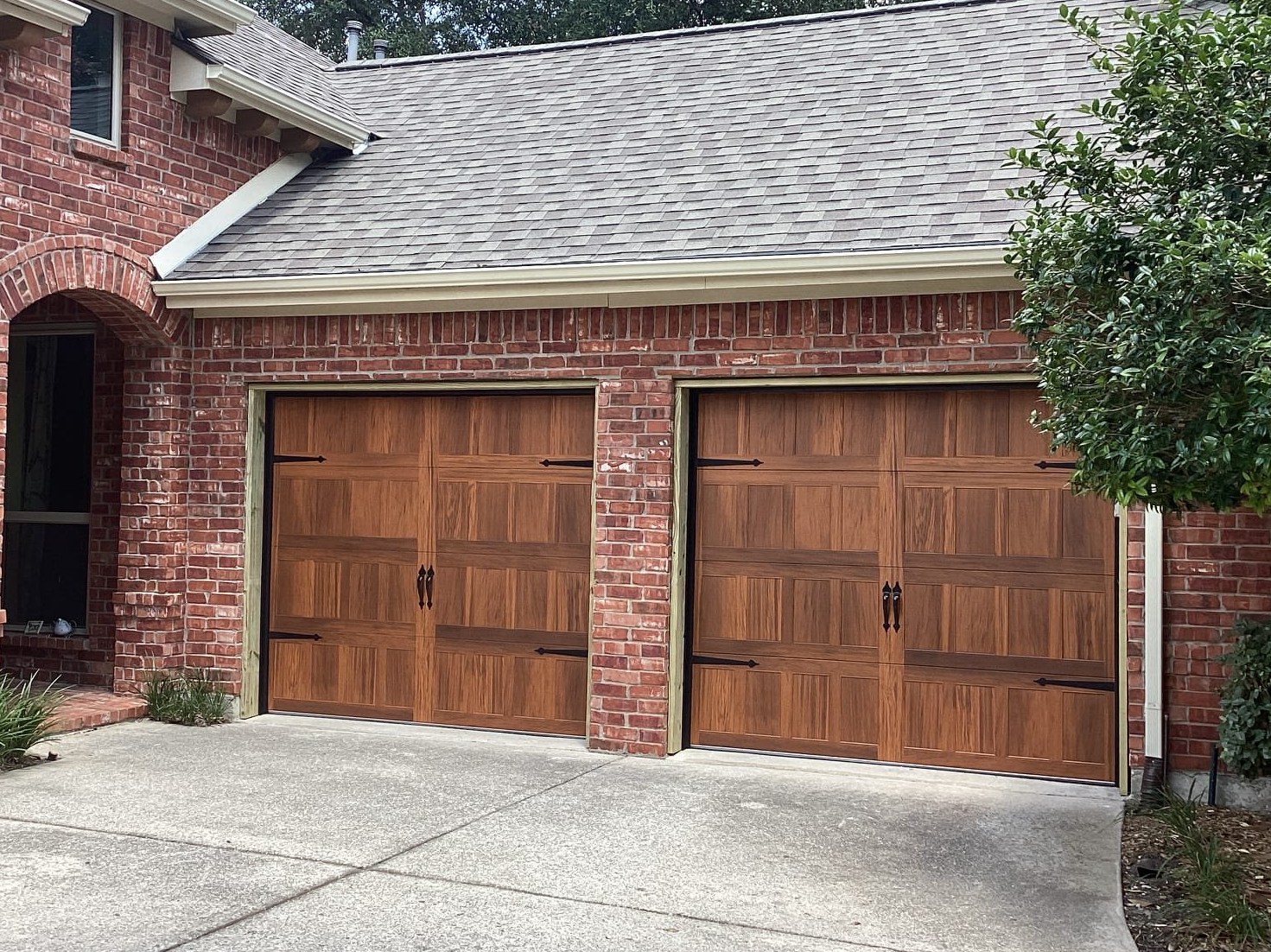 Brick house with brown, paneled garage doors. Gray roof and concrete driveway.