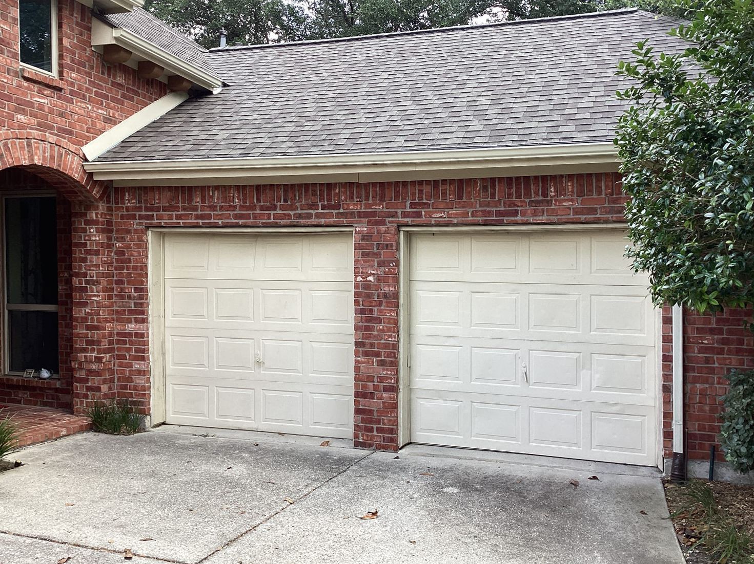 Two-car garage with white doors, brick exterior, and gray shingle roof.