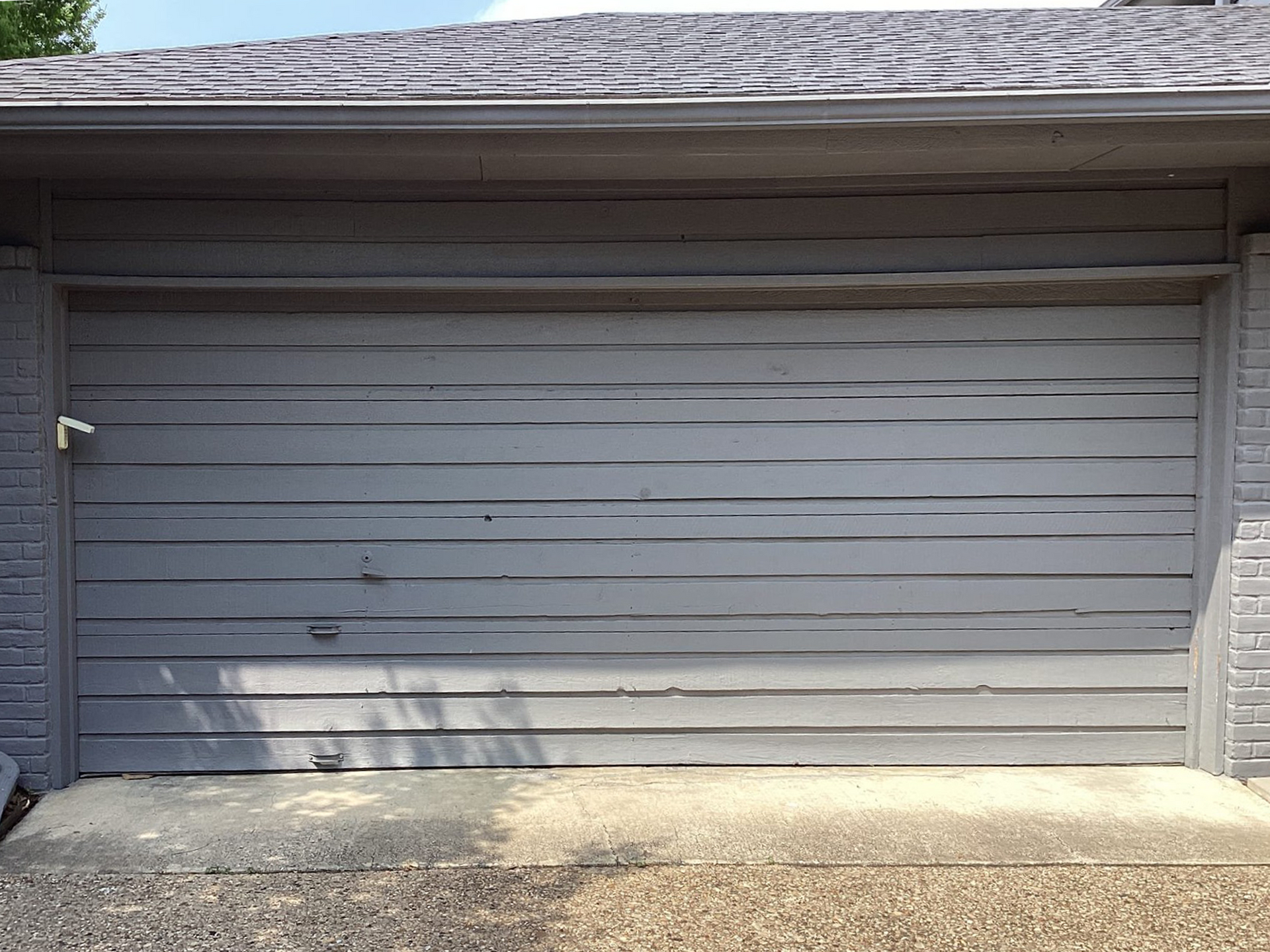 Gray wooden garage door with weathered paint, in front of a concrete driveway.