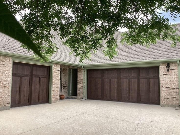 Brown garage doors on a brick house with a concrete driveway, under a leafy tree.