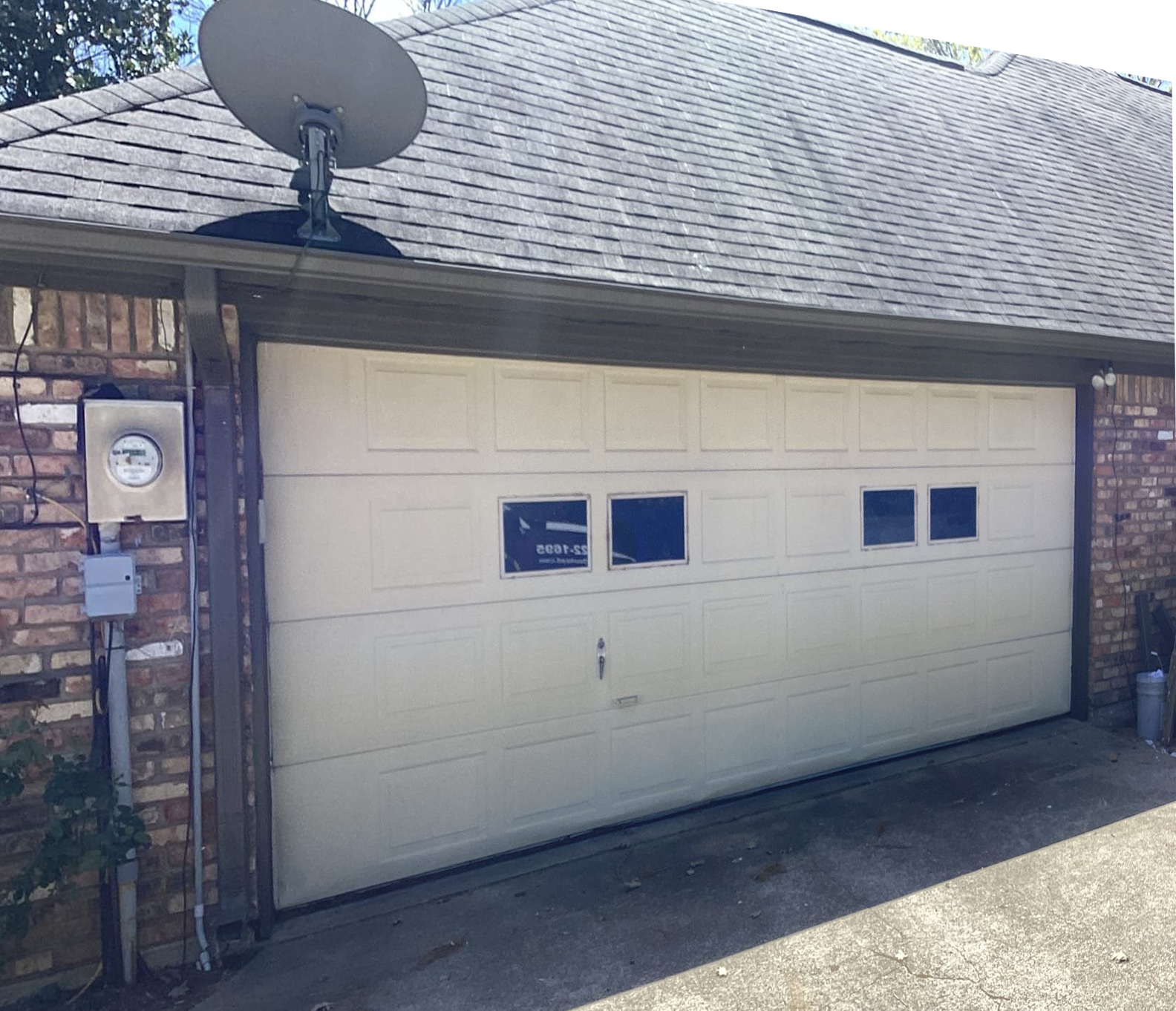 Tan garage door with small windows, satellite dish on roof, brick building.