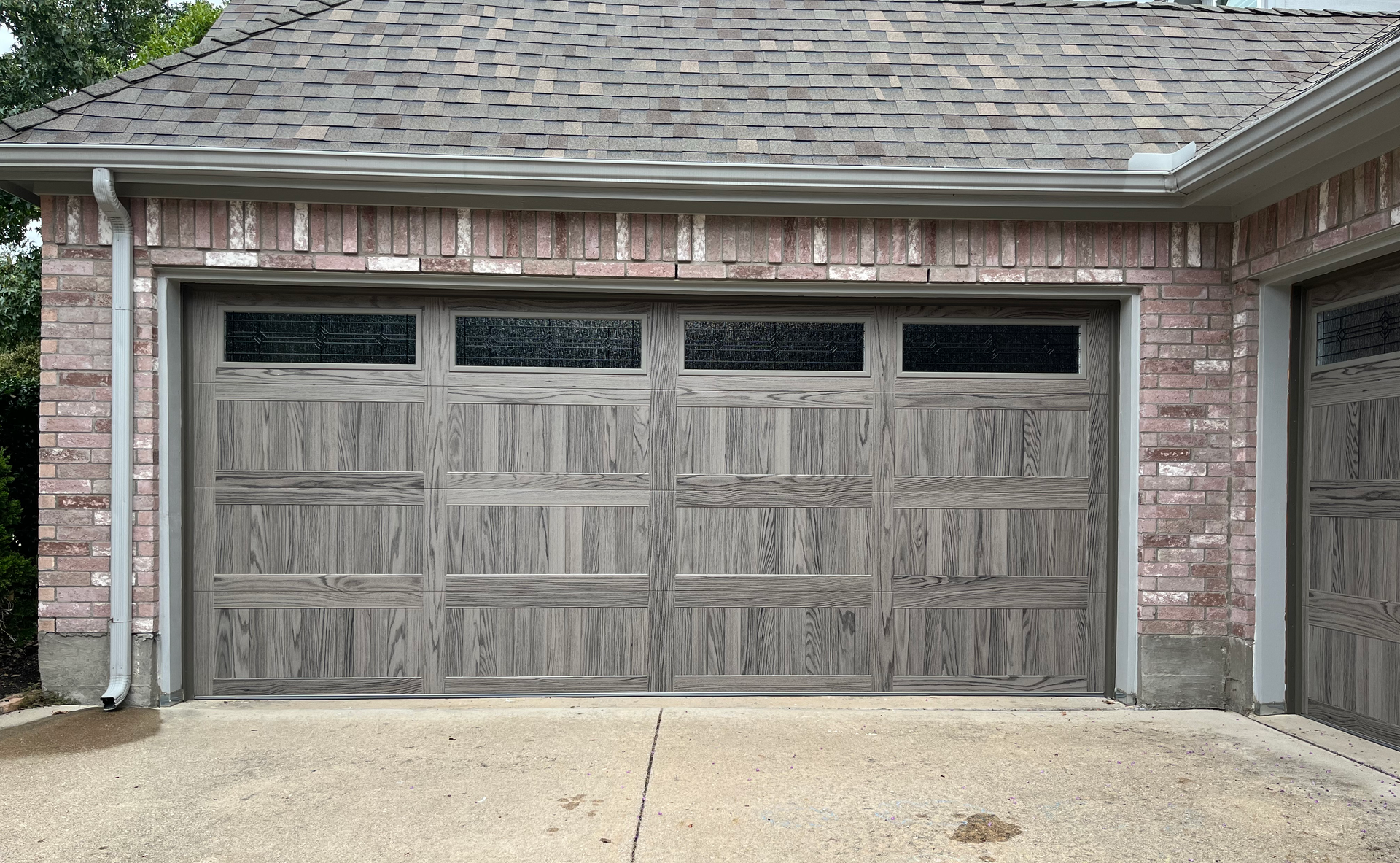 Gray garage door with frosted windows, brick facade, and concrete driveway.