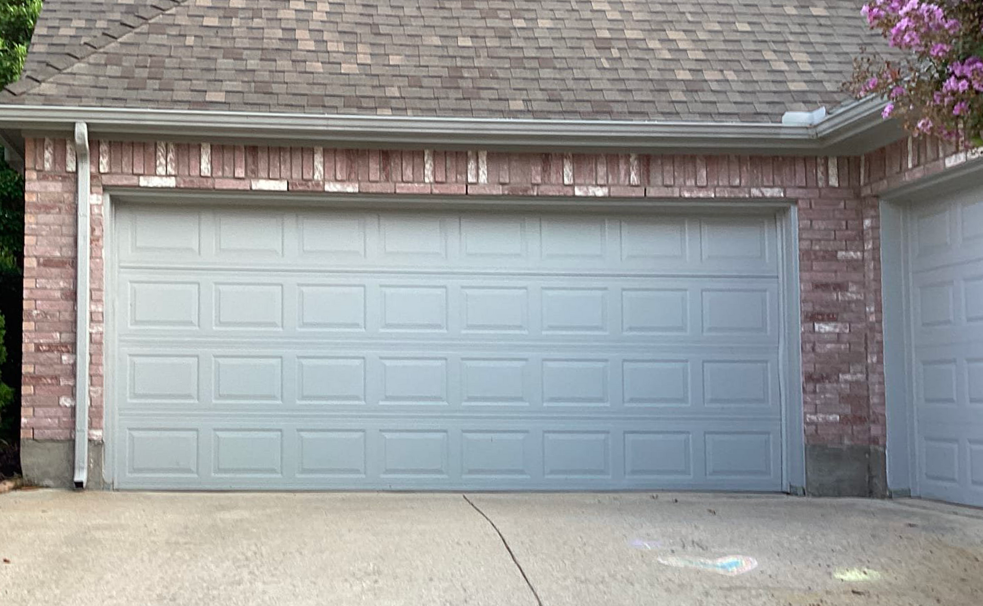 Gray garage door on a brick building with a concrete driveway.
