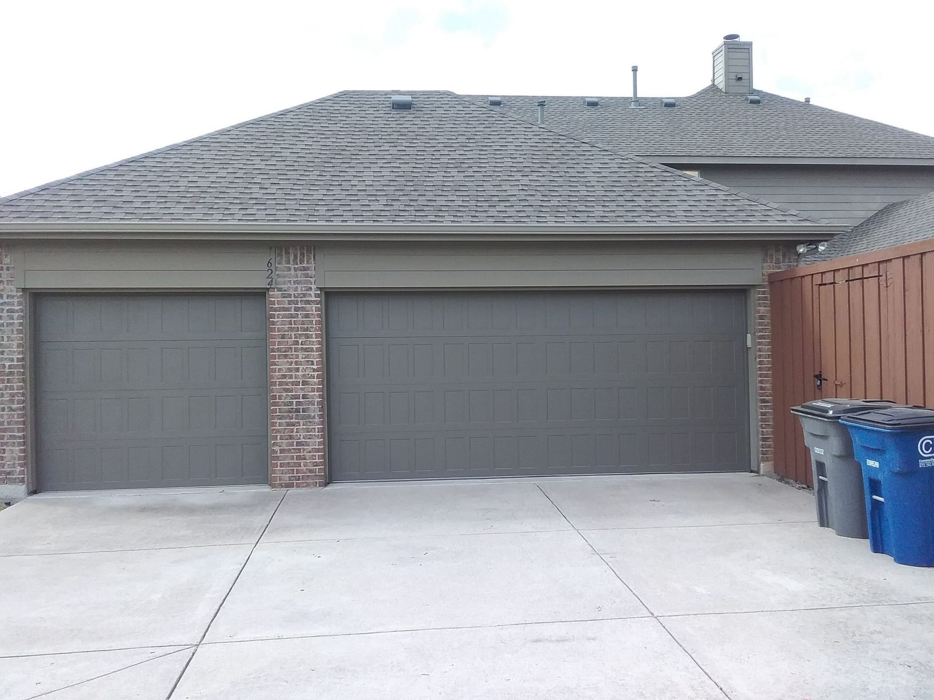 A house exterior featuring a two-car garage with dark gray doors, brick accents, and trash bins parked on the side.