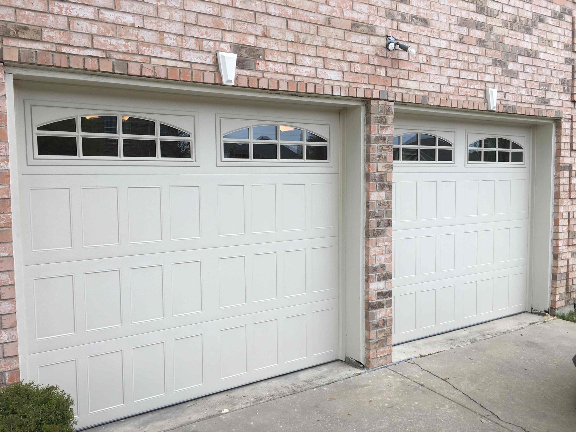 Two cream-colored garage doors with arched windows at the top, set into a brick exterior wall.