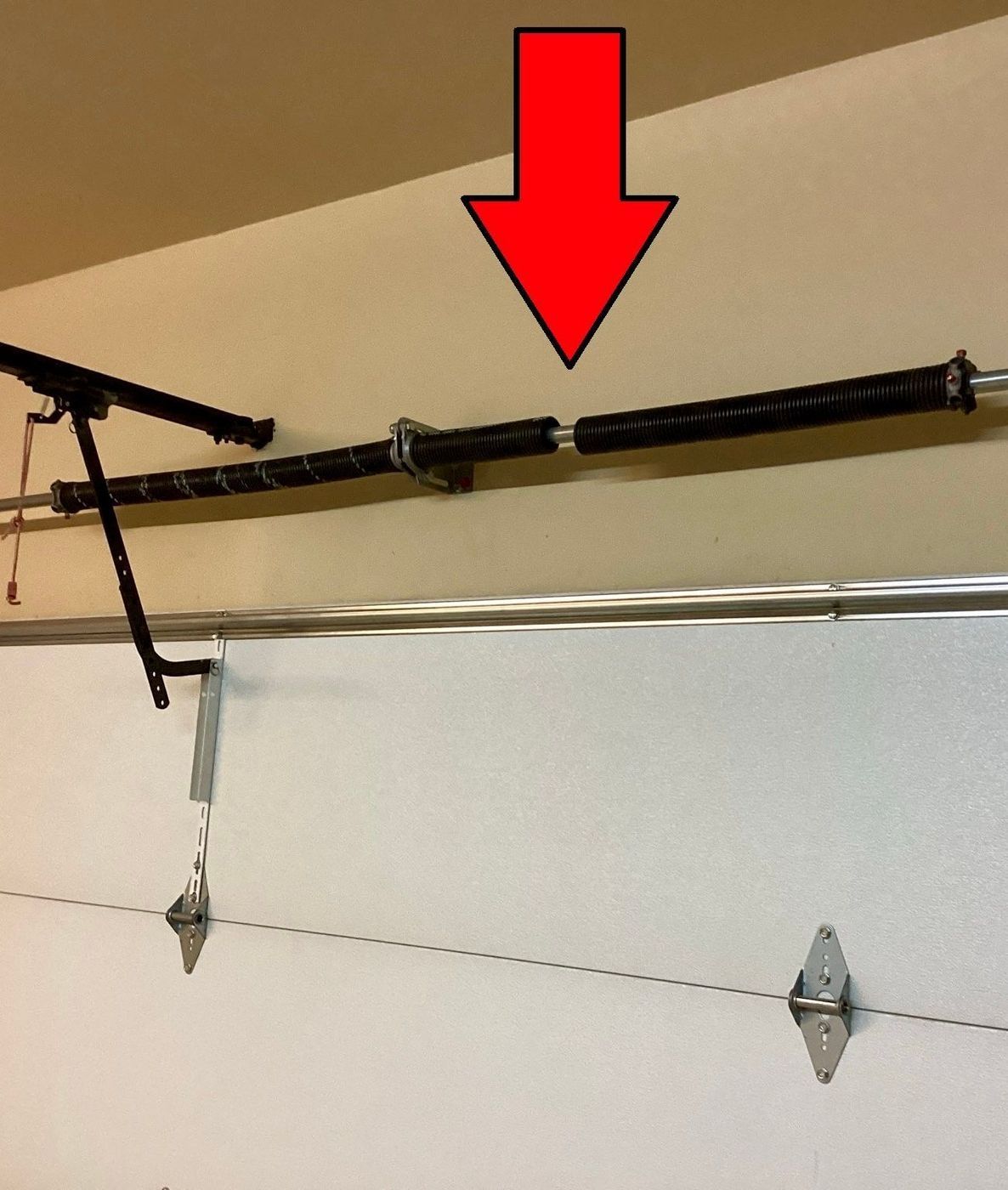 Broken garage door spring with red arrow pointing to the break.