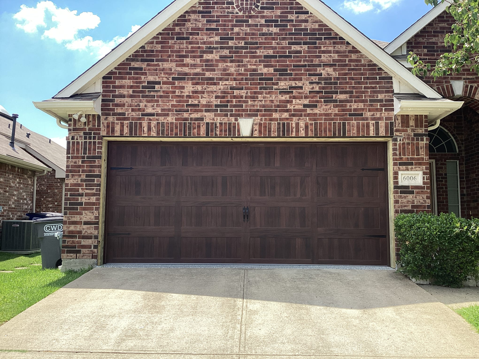 Brown garage door under a brick house with a concrete driveway.