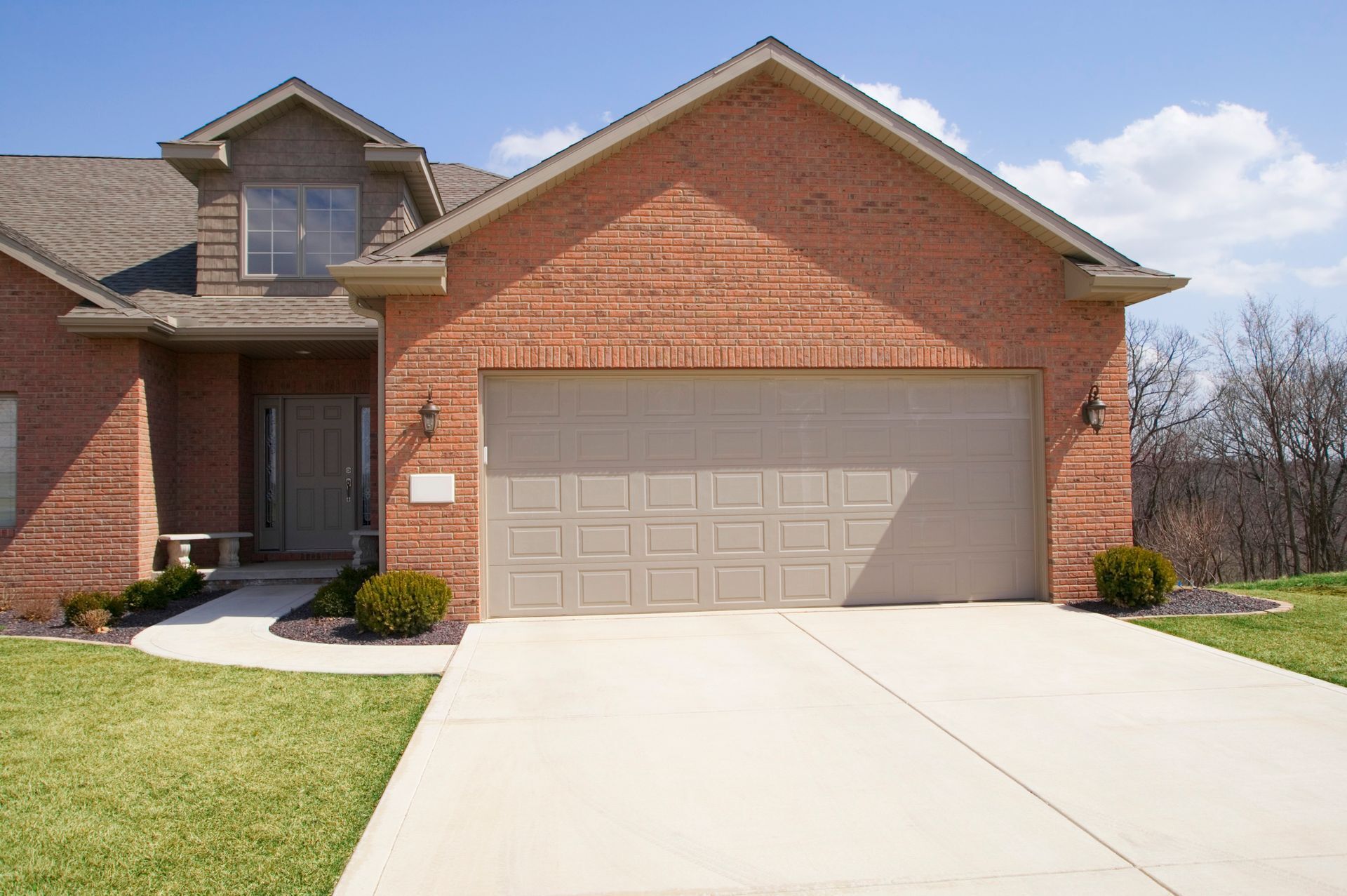 Brick house with beige garage door and concrete driveway on a sunny day.