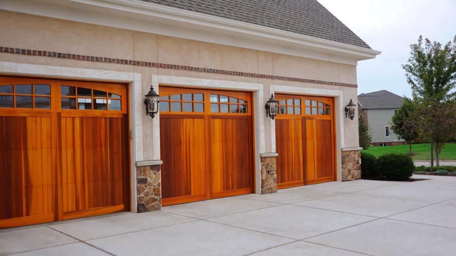Three wooden garage doors with windows in a light-colored stone and stucco home exterior.
