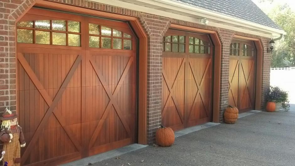 Three wooden carriage-style garage doors on a brick building, with pumpkins placed on the driveway.