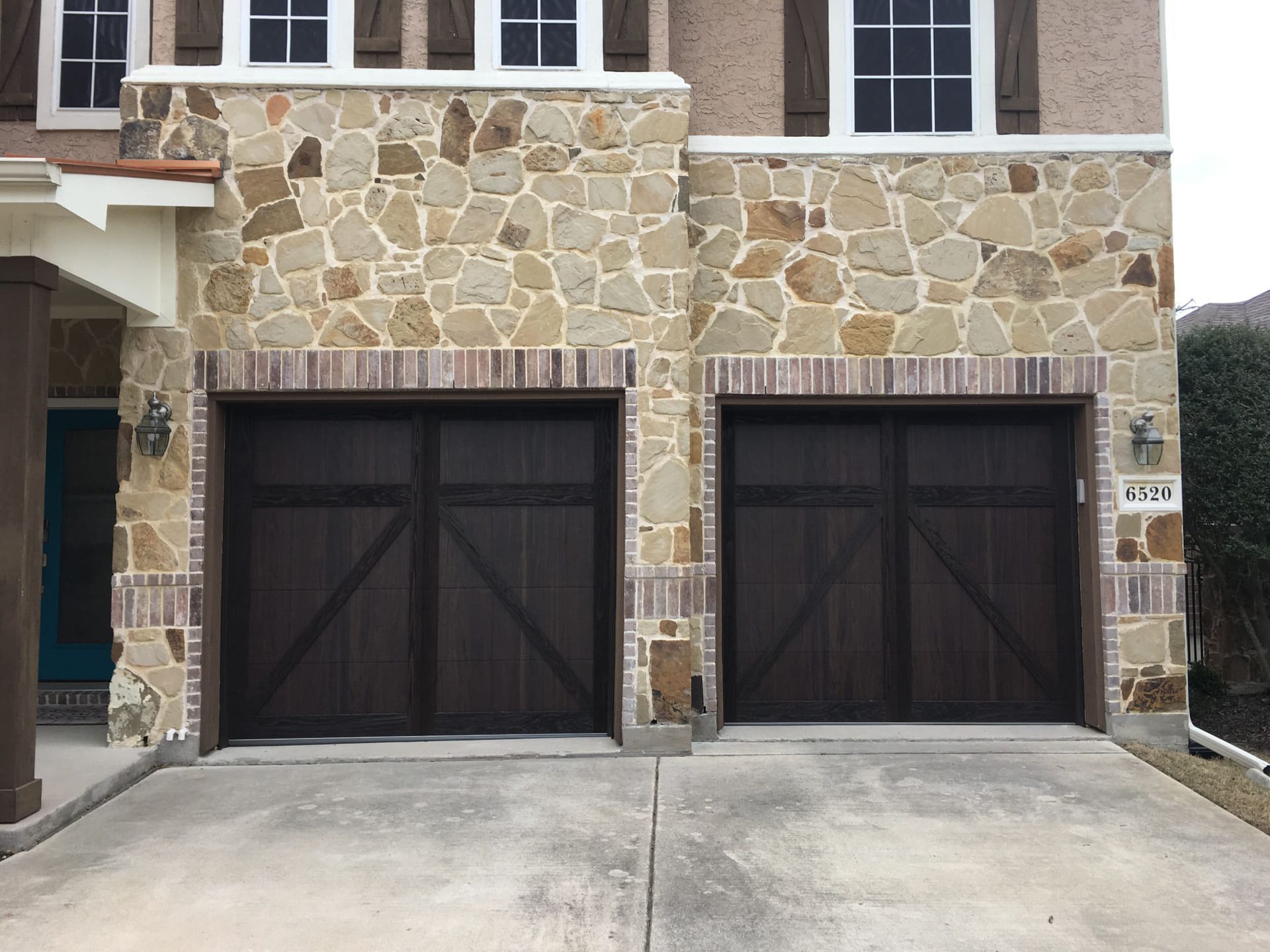 Two brown garage doors framed by stone and brick on a house with a concrete driveway.
