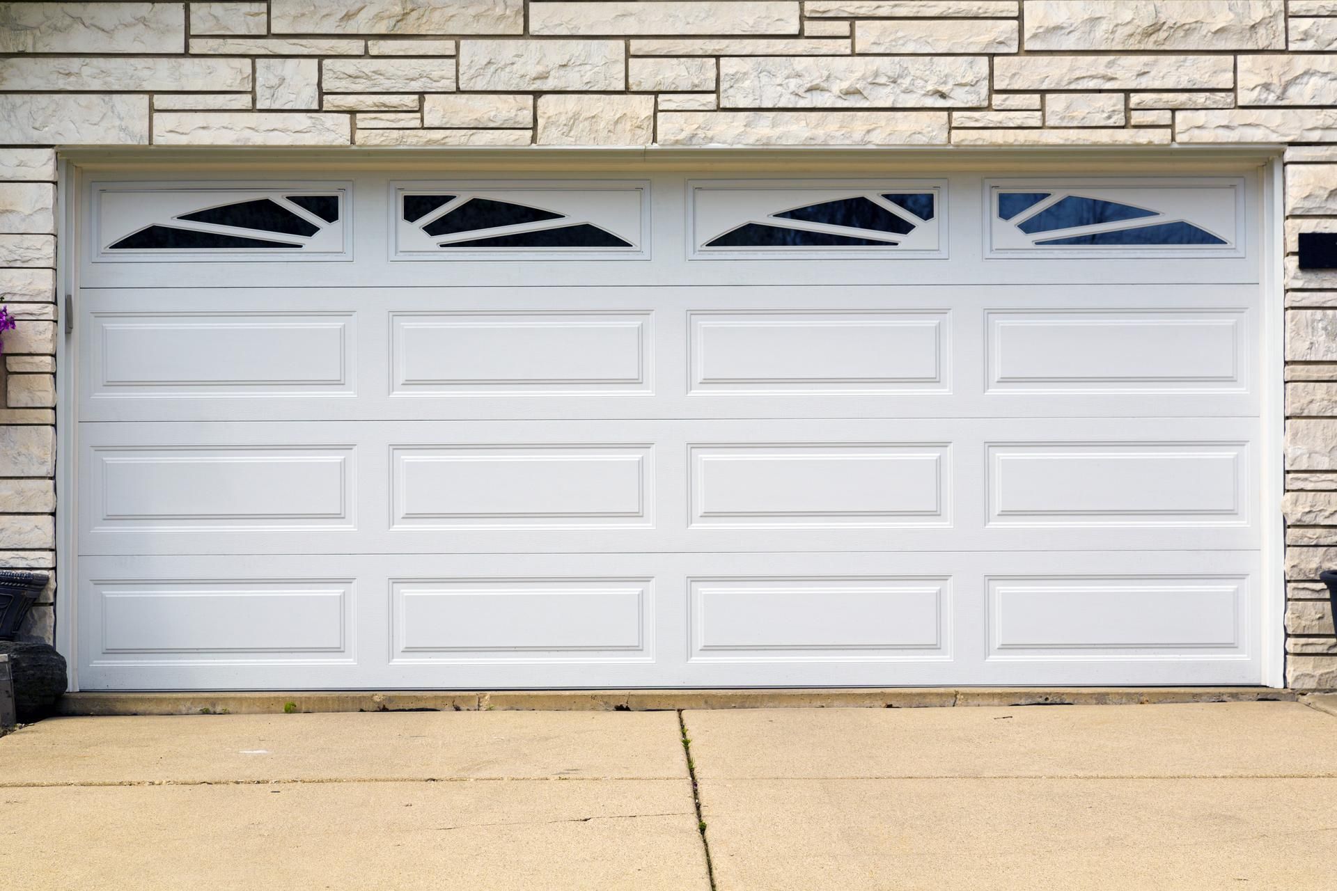 White garage door with geometric windows, in front of a tan brick wall.