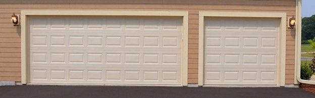 Two beige garage doors on a tan house with a dark driveway.
