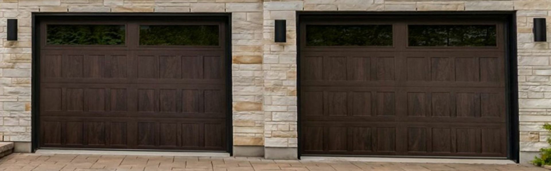 Two dark brown garage doors with glass panels, set in a stone wall, with exterior lights.