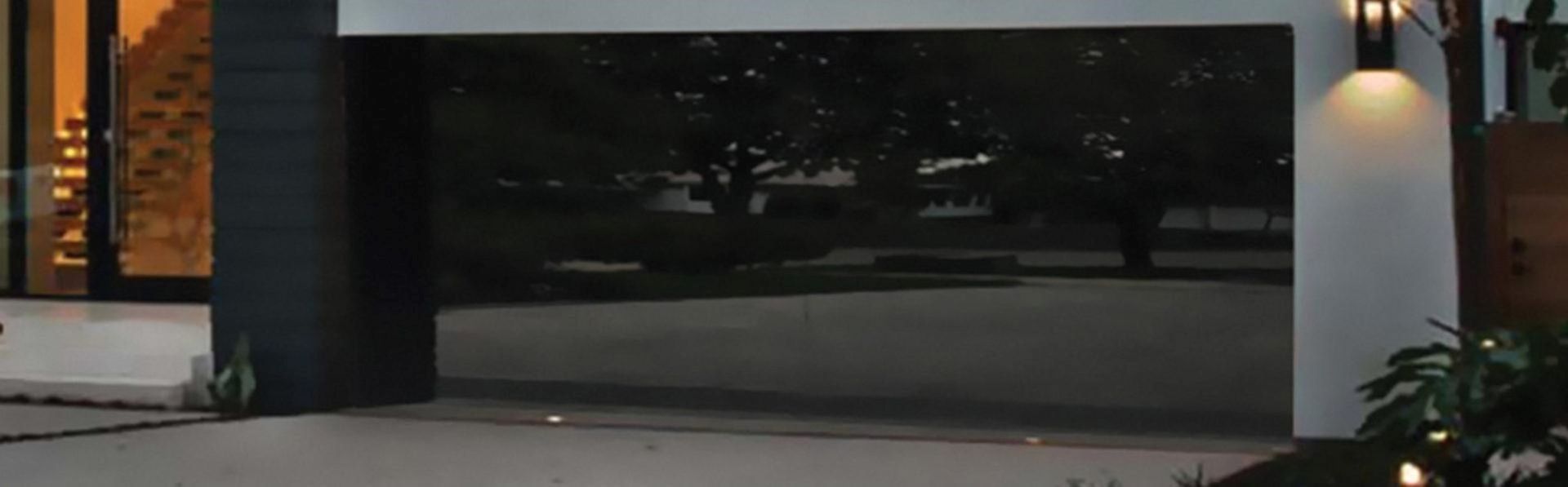 Modern house exterior with dark reflective garage door and warm lighting.