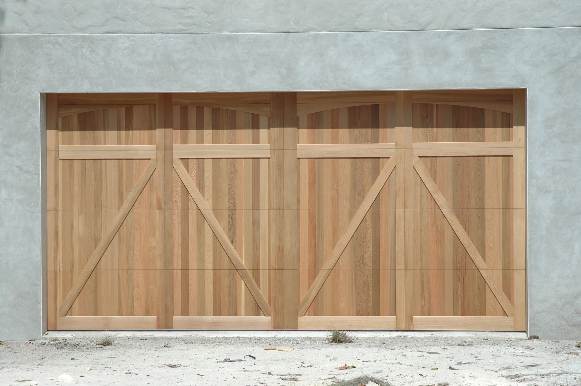 A modern wooden garage door with a diagonal brace pattern set against a light gray concrete wall.