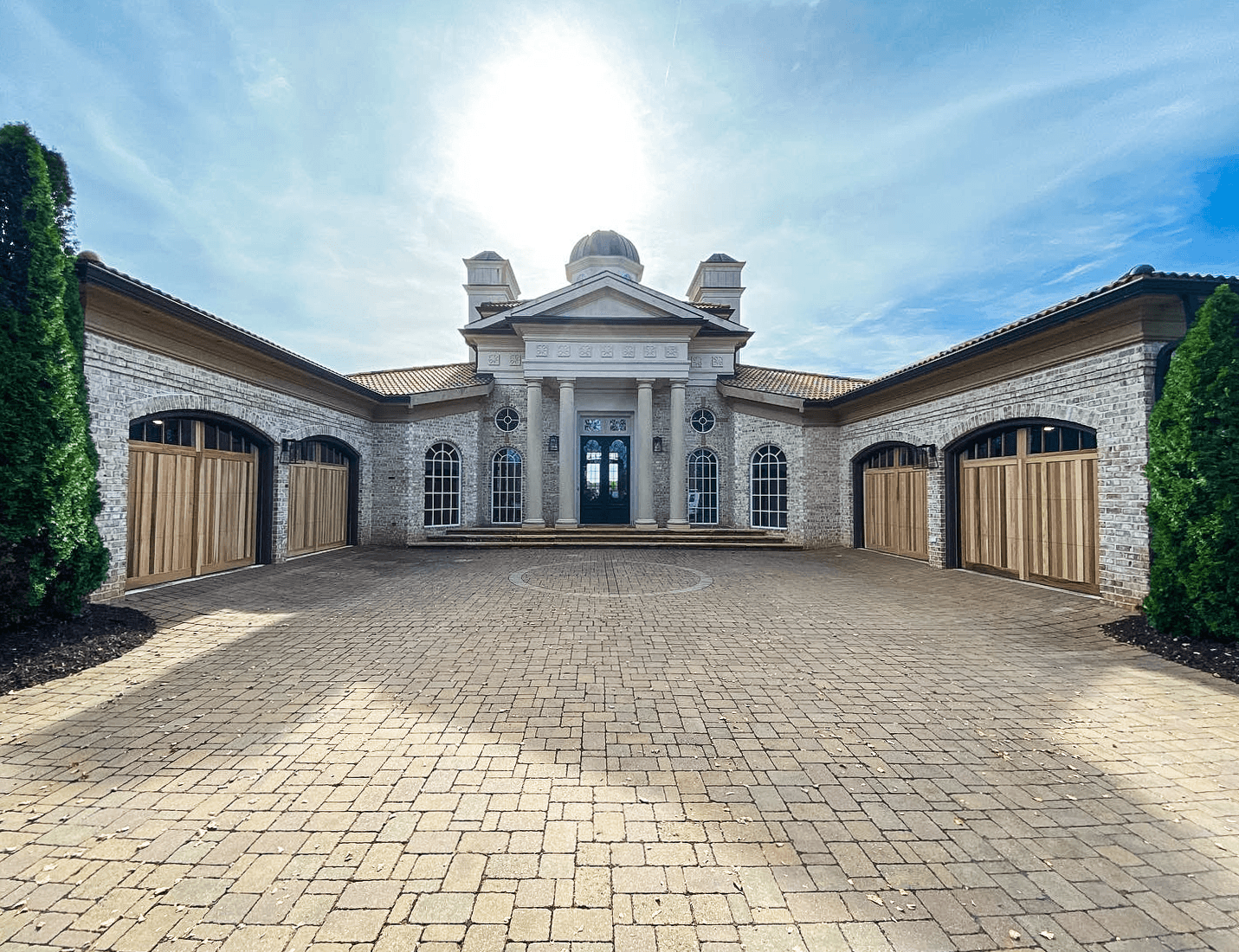 A grand, light-colored stone mansion with a central domed entrance and flanking garages surrounding a brick courtyard.