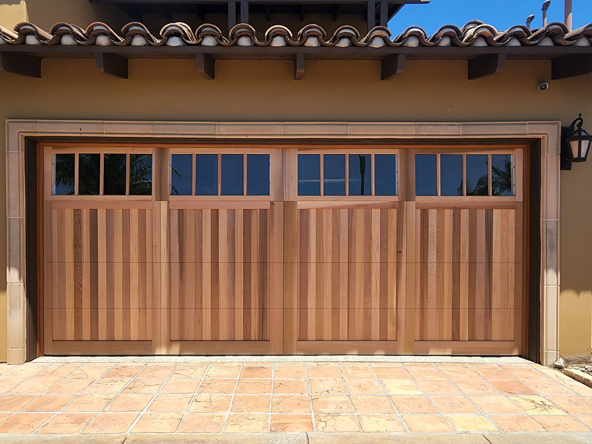 A wooden four-panel garage door with rectangular windows above, set in a tiled, Spanish-style home exterior.
