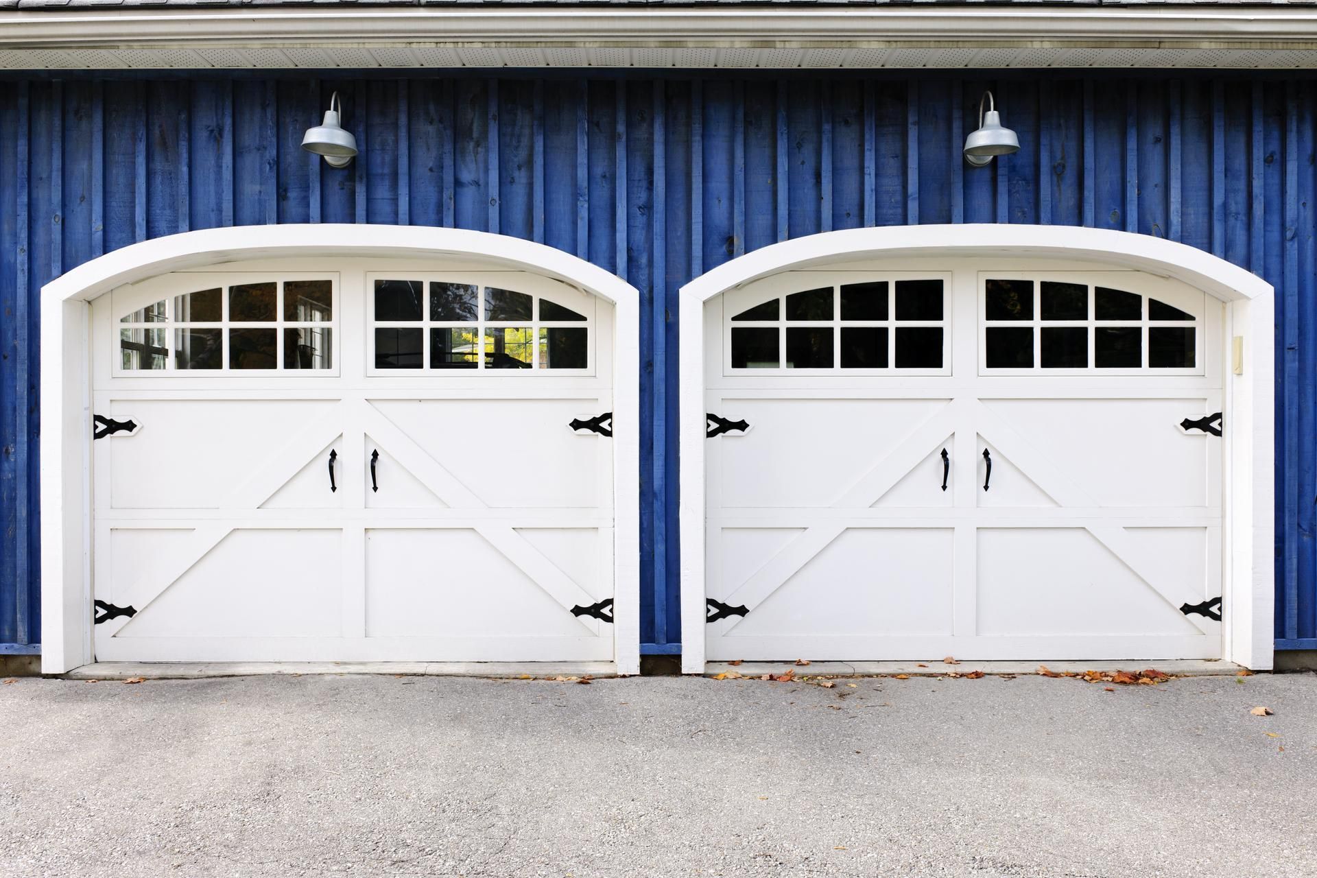 Two white garage doors with arched tops, black hardware, and blue building exterior.