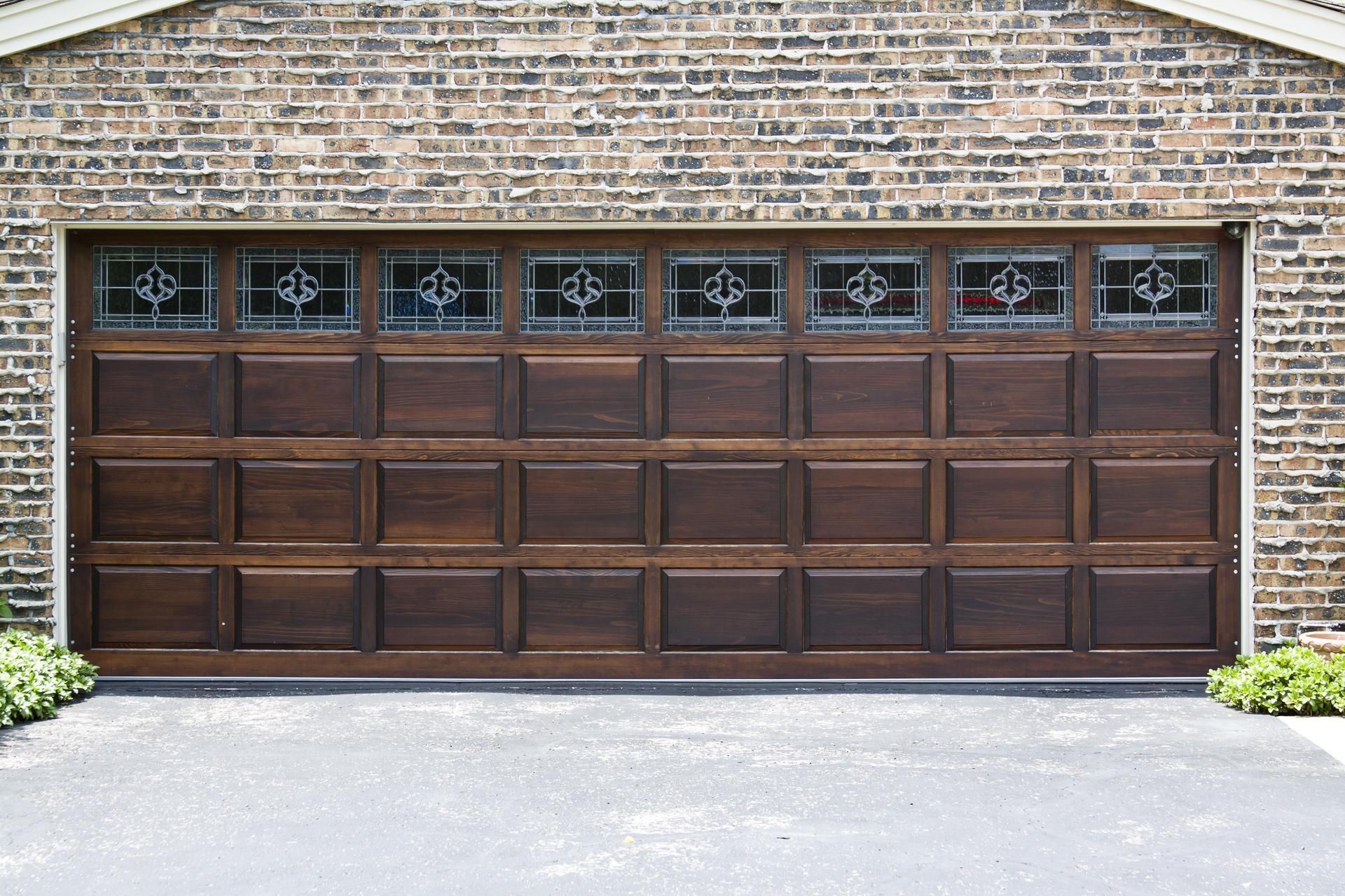 Brown garage door with decorative glass panes against a brick building.