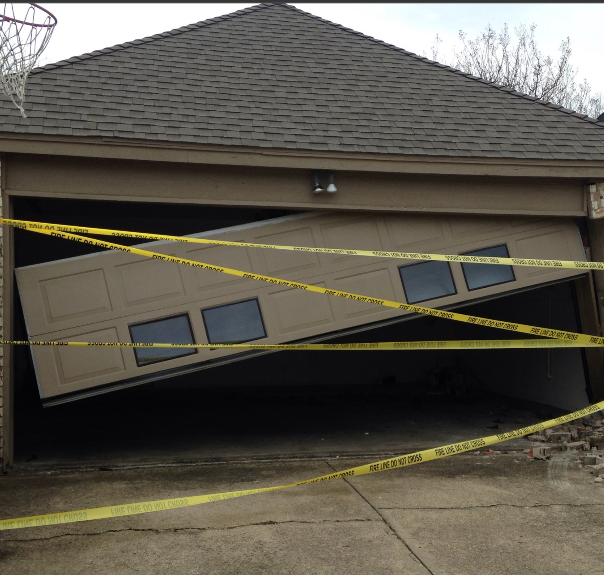 Damaged garage door, tilted and partially open, with yellow caution tape.