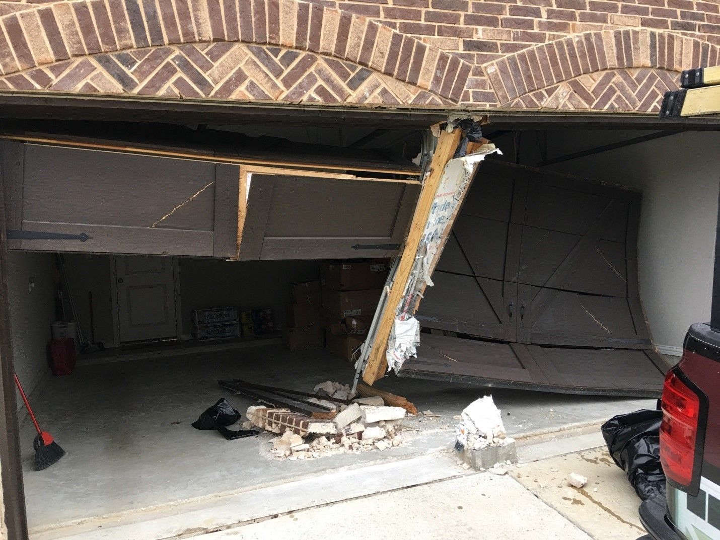 Damaged garage door, partially collapsed. Debris on concrete floor. Brickwork arch above.