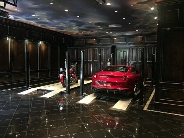 Luxury garage with a red Ferrari and a motorcycle on lifts, under a painted celestial ceiling.