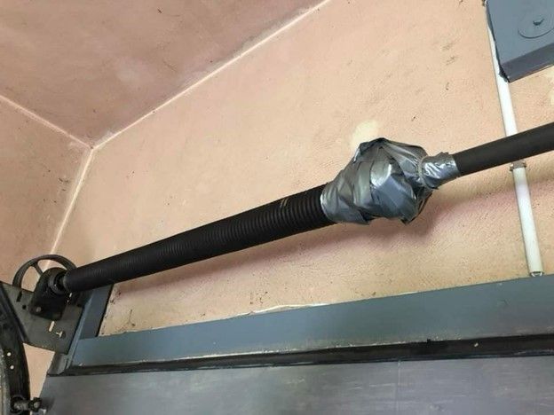 Garage door torsion spring, duct taped. Black spring on a metal bar, mounted in a garage.