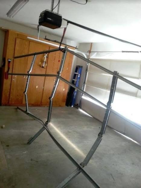 Metal frame structure in a garage with wooden storage cabinets and a garage door opener.