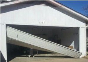 White garage door partially open, appearing damaged and leaning at an angle.