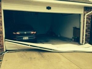 Damaged garage door, partially open with a car inside. The door is bent and crumpled on the ground.