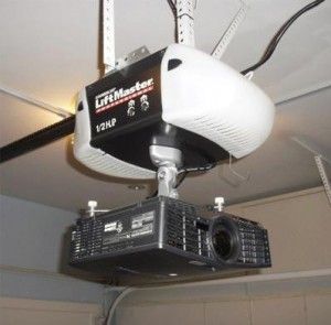A projector mounted under a garage door opener. The projector is black, the opener is white.