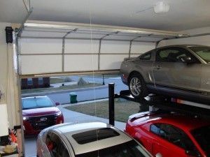 Garage with cars; one on a lift, others parked inside and outside with garage door partially open.